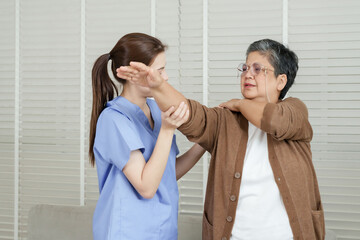 Asian female physiotherapist supporting senior woman in shoulder rotation motion during rehabilitation exercise to reduce stiffness and increase flexibility in upper body therapy