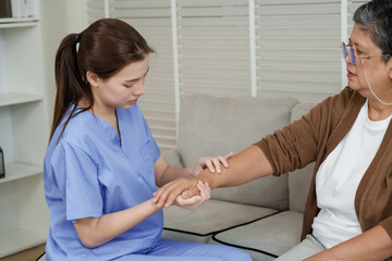 Obraz premium Female therapist examining elderly asian woman’s arm by pressing and feeling muscle tension during physical therapy session on sofa in clinic environment with focus on recovery