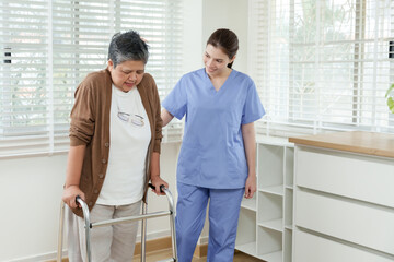 Obraz premium Young asian female physiotherapist encouraging senior asian woman walking with walker at home focusing on physical therapy progress and mobility support for elderly care rehabilitation