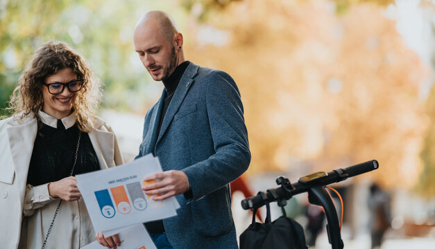 Two professionals examine charts and documents outdoors in autumn, standing beside a scooter. Warm colors and relaxed mood convey collaboration, planning, and a friendly professional connection.