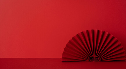 Side view of a red studio scene with a folded paper fan on a flat surface, symbolic of Chinese New...