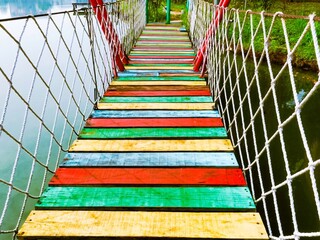 Close-up of a colorful suspension bridge over a lake. A colorful wooden suspension bridge.
