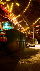 Naklejka premium A carnival ride with bright lights illuminates the night at an abandoned amusement park, showcasing a nostalgic yet eerie scene.