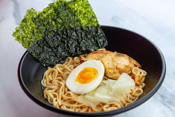 Ramen with egg noodles, char siu chicken, and fresh pickles, in a savory broth on a light background