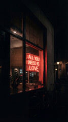 Neon love sign glowing through a rainy café window at night.