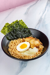 Ramen with egg noodles, char siu chicken, and fresh pickles, in a savory broth on a light background