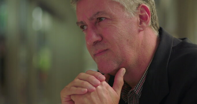 Close-up of middle aged man in office lounge with tense expression and clasped hands, conveying regret, worry, and inner anguish in quiet workspace