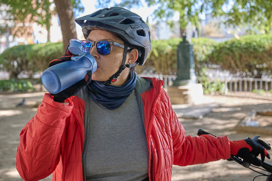 Close-up of woman wearing helmet and sunglasses drinking water during outdoor cycling.