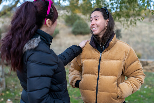 Woman talking and smiling with friend outdoors, receiving shoulder support while wearing a warm coat