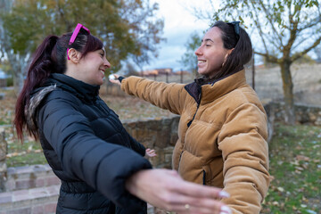 Two smiling women friends stretching arms for a warm welcome hug outdoors on an autumn day