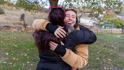 Happy young women friends embracing outdoors, sharing a warm reunion moment with genuine laughter and affection