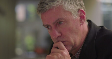 Close-up of middle aged man resting chin on hand in office lounge, deep in thought and focused on...