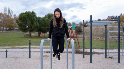 Woman performing a workout on parallel bars, building body strength and working on physical conditioning in a public exercise park