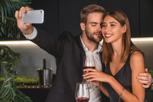 Joyful young couple taking selfie while having romantic dinner at home. Proposal for social media. Anniversary celebration and posting on Internet online in restaurant indoors