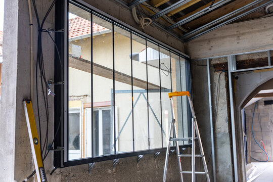 Gros plan sur une grande verri&egrave;re install&eacute;e dans un b&acirc;timent en travaux, r&eacute;v&eacute;lant la structure m&eacute;tallique, le vitrage et l&rsquo;avancement du chantier.