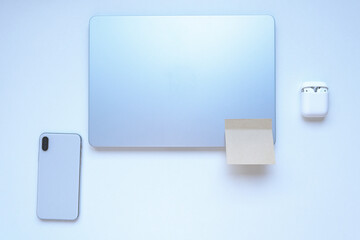 Top view of a clean minimal workspace with a closed laptop, smartphone and wireless earbuds on a white background. Modern tech flat lay with copy space.