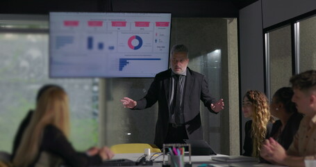 Corporate executive presenting key data insights to engaged team during business meeting in modern boardroom with large display screen