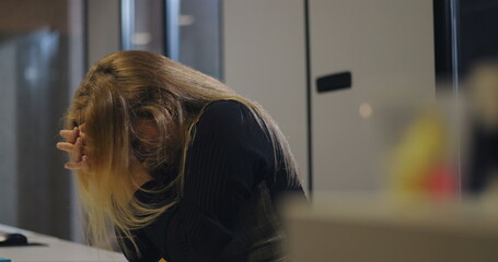 Close-up of overwhelmed middle-aged woman burying head into arms at office table, exhibiting signs...