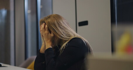 Close-up of overwhelmed middle-aged woman burying head into arms at office table, exhibiting signs...