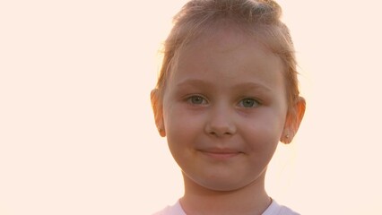 Portrait smiling cute little girl posing outdoor at sunset sky closeup. Happy face of adorable female child kid relaxing enjoy childhood with positive emotion at evening morning outside nature