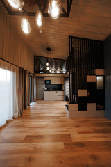 A compact loft interior shows wood floors, glass pendants, matte black accents, and a cube shelf stair to a mezzanine with metal railing. Evening light filters through drapes.
