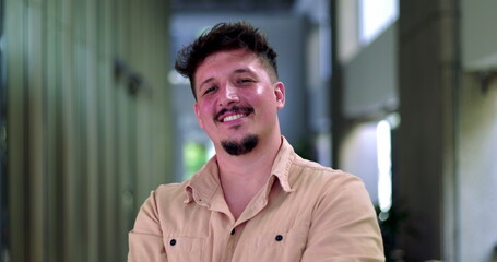 Obraz premium Close-up of smiling man with short hair and facial hair in modern office hallway, arms crossed and exuding confidence and warmth