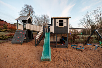 Custom wooden playset in a private yard at late afternoon shows green slide, rope climbing wall,...