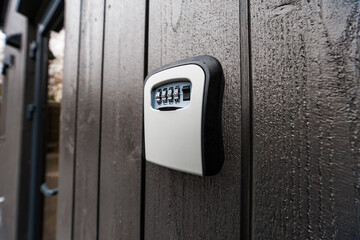 Close up of a wall mounted combination key safe on dark stained vertical wooden planks in daylight....