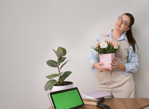 Office setting with a businesswoman in a beige suit holding festive flowers for March 8. Digital tablet with green screen for mockup on a clean workplace surface - Powered by Adobe
