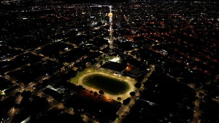 Aerial night view of an illuminated stadium with running track and city skyline. Sports, architecture, night. Perfect for sports, architecture, commercial themes.