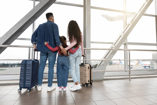 A family stands at the airport terminal, gazing out the large windows at the planes outside. Their excitement and anticipation are evident as they prepare for their journey.