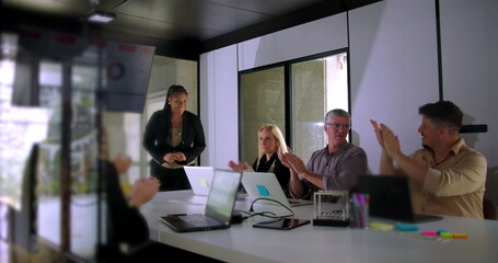 Colleagues applauding African American presenter after presentation in bright modern conference room with laptops and digital charts