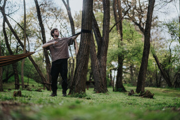 A man in casual clothing stretches beside a hammock tethered between trees in a tranquil forest. The scene captures outdoor relaxation, nature connection, and the peaceful mood of a woodland park.