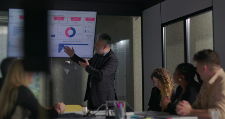 Confident business leader delivering passionate presentation to engaged colleagues during corporate meeting with data charts on screen