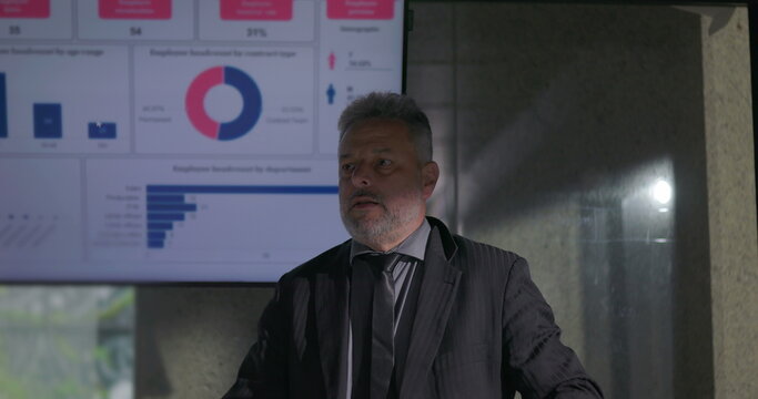 Confident business leader delivering passionate presentation to engaged colleagues during corporate meeting with data charts on screen - Powered by Adobe