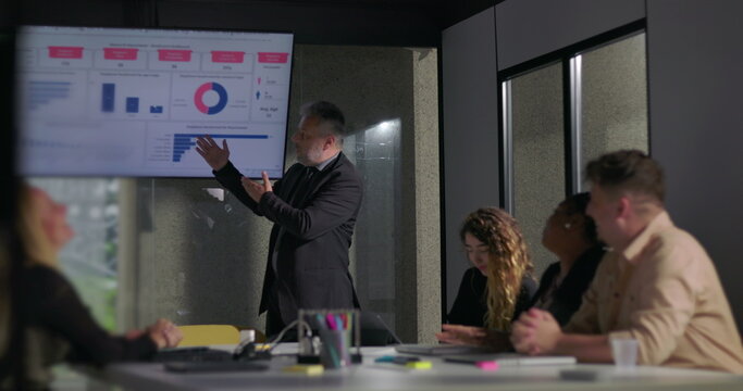 Confident business leader delivering passionate presentation to engaged colleagues during corporate meeting with data charts on screen