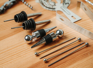Close-up of stainless-steel liquor pourers, bottle stoppers, and cocktail picks arranged on a wooden table Detailed view highlighting premium bar accessories for precise pouring and drink presentation