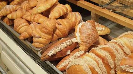Variety of freshly baked pastries, croissants, sweet rolls arranged in bakery or cafe display window. Grocery store setting, highlighting artisanal bread and inviting breakfast, brunch and dessert