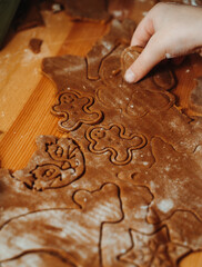 Close-up of gingerbread dough with various festive shapes cut out—gingerbread men, hearts, stars, and animals. A child’s hand lifts the dough, capturing a warm homemade Christmas baking moment.
