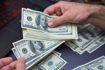 Close-up view of hands sorting multiple 100 bills on a dark desk, illustrating money handling, finance tasks, budgeting, and cash operations.