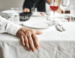 An aged hand rests gently on a pristine white tablecloth, awaiting a meal at an elegant dinner