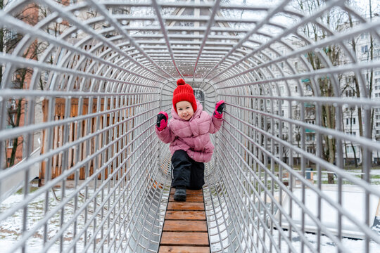 A little child girl in a hat plays on the playground in winter with snow - Powered by Adobe