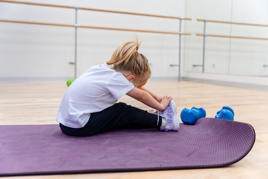 Caucasian child girl 3 year sitting on a mat doing stretching in the gym