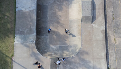 Aerial view of a concrete skatepark bowl where a group of skaters gather near the edge. The image highlights urban sports, outdoor recreation, and youth culture.