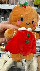 Adorable Plush Gingerbread Girl Toy in Red Dress with Holiday Details Held in Hand – Cute Christmas Stuffed Cookie Character on Store Shelf