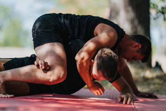 Two men grapple on a red mat in a park, showcasing strength and teamwork during an outdoor training session. Intense grip, focus, and athleticism highlight a dynamic fitness moment. - Powered by Adobe