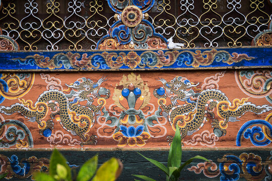 View of intricate dragon murals dance across the weathered facade of Kyichu Lhakhang, under ornate latticework, in Paro, Bhutan.
