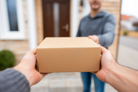 POV of caucasian hands receiving cardboard package from delivery man at front door of house