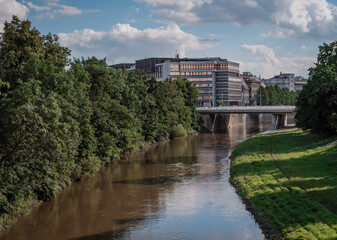 River flows smoothly beside urban buildings under a clear blue sky in the afternoon