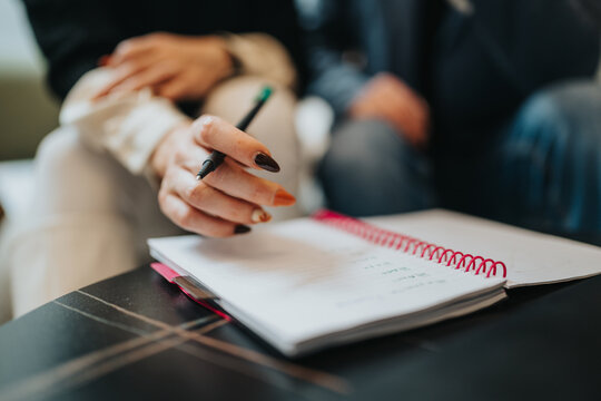 Two colleagues sit across from each other, focused on a spiral notebook as one hand writes with a pen. A moment of planning, collaboration, and professional discussion in a modern office.